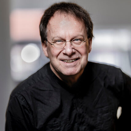 Dozent Peter Holtslag. Lächelnd mit schwarzem Hemd in Frontansicht. Hintergrund ist unscharf.